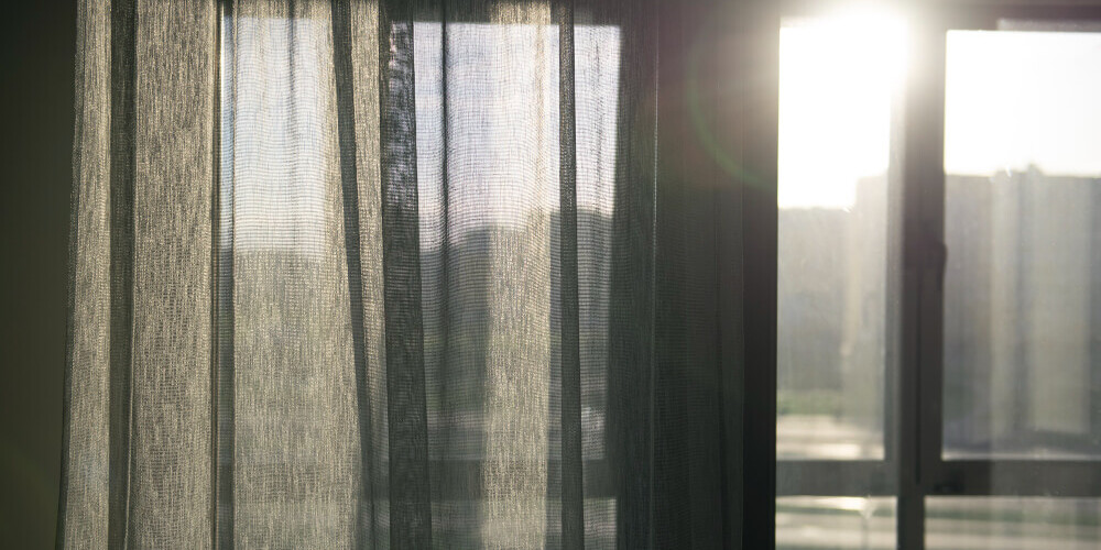 Sole al tramonto attraverso una tenda semitrasparente che copre una finestra.