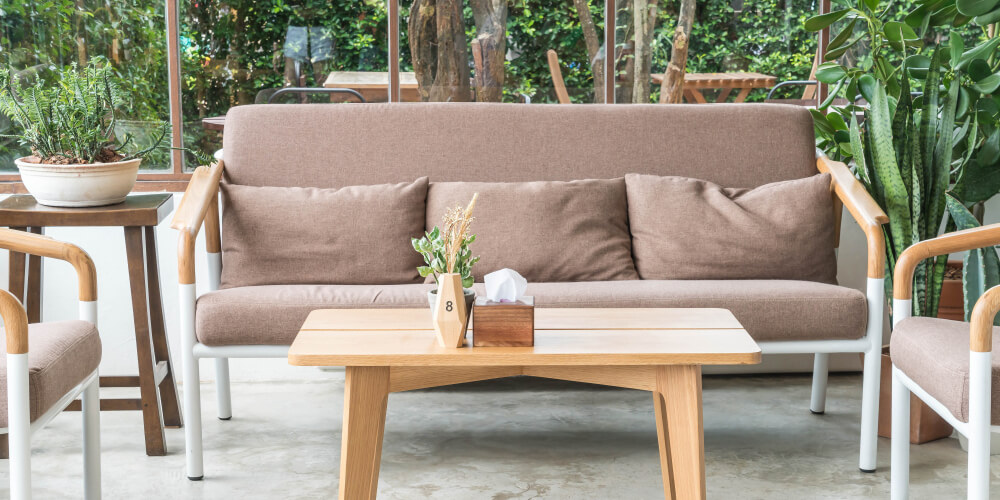 Sofà marrone chiaro, due poltrone, tavolino e piante verdi interne.