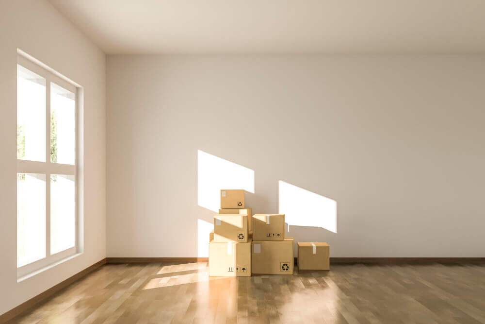 Scatole di cartone in una stanza vuota con pavimento in legno e luce solare.