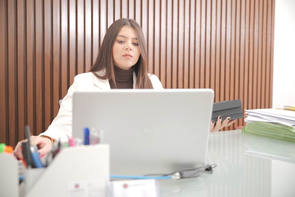 Donna con giacca bianca e maglia marrone lavora al computer.