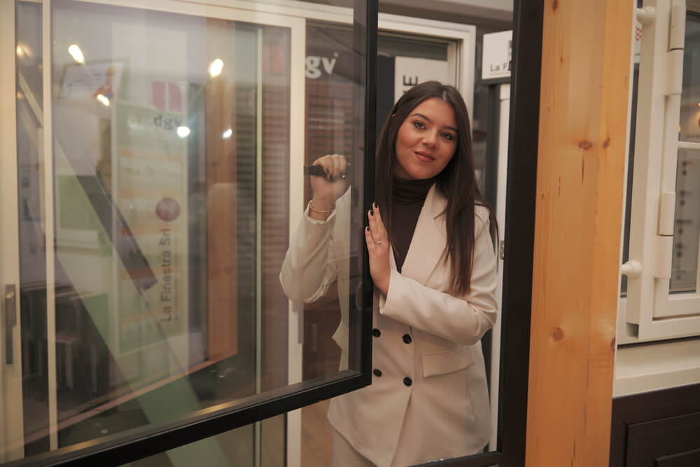 Una giovane donna sorridente, in abito beige, regge una finestra aperta.