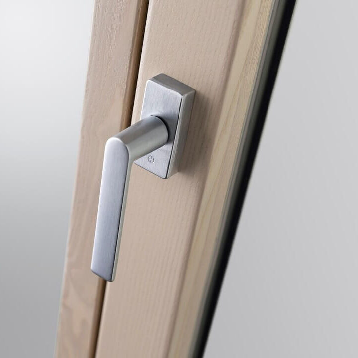 Maniglia moderna in metallo satinato su cornice di finestra in legno chiaro.