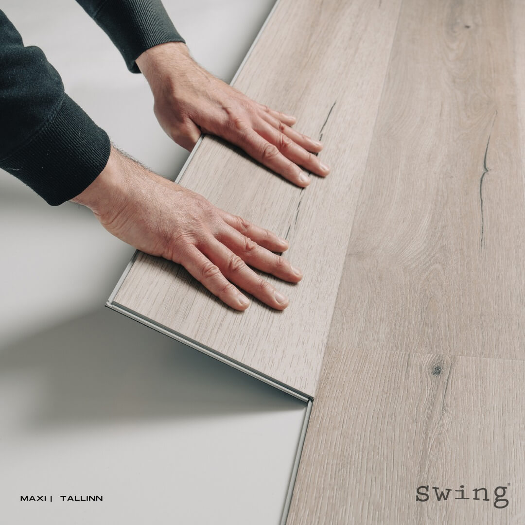 Mani che posano un pannello di pavimento laminato color legno chiaro.