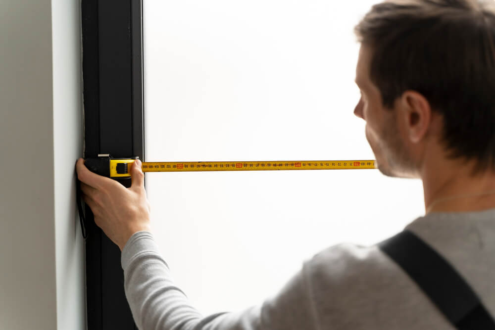 Un uomo misura con un metro a nastro giallo una porta o finestra.