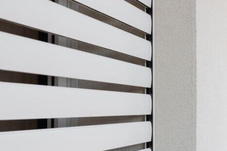 Tapparelle bianche moderne che schermano una finestra, con una parete adiacente grigio chiaro.