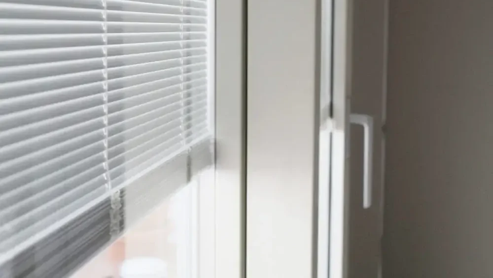 Dettaglio di persiane orizzontali bianche installate su una finestra, con una maniglia visibile.